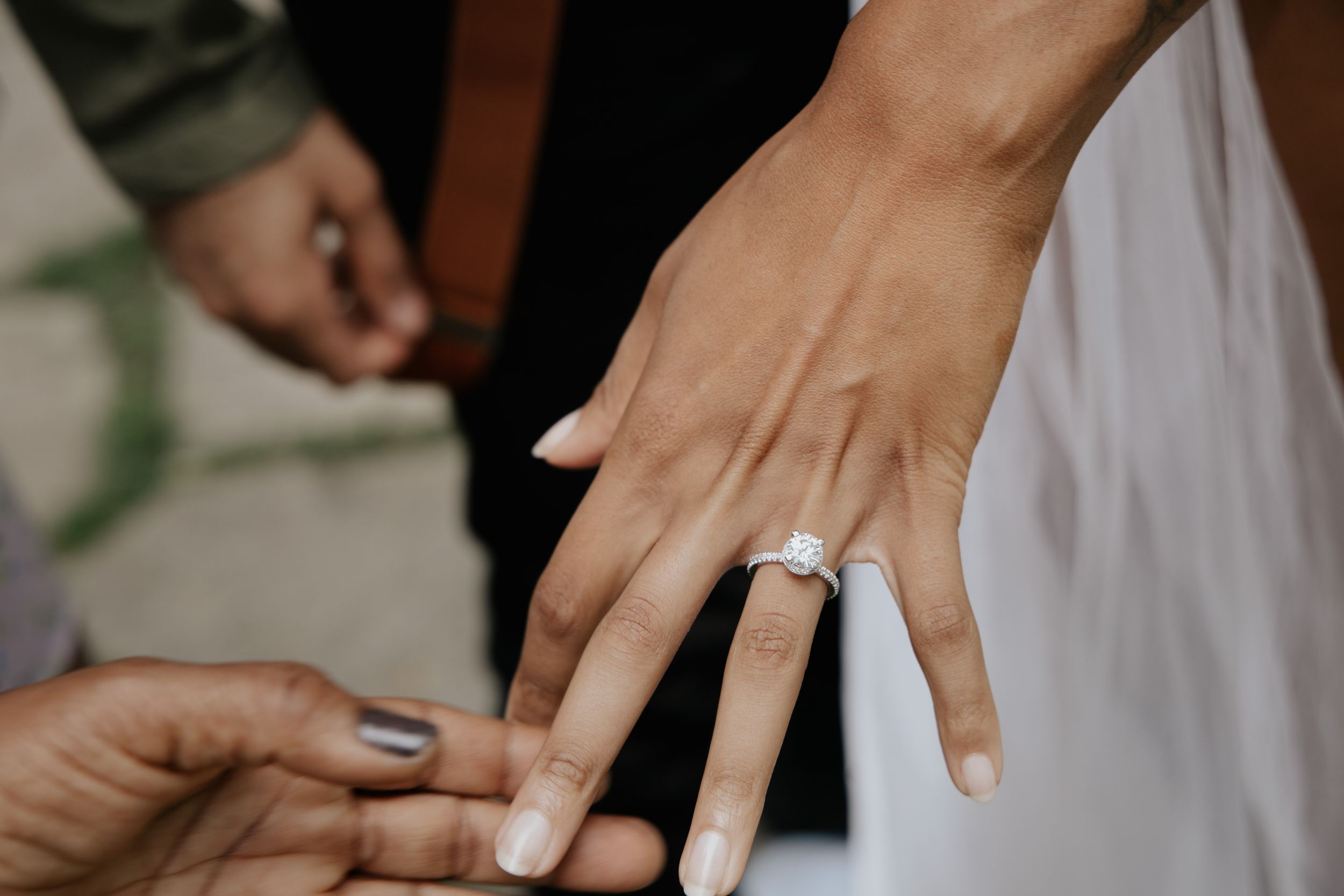 Close-up detail shot of a sparkling engagement ring on a hand with white manicured nails.