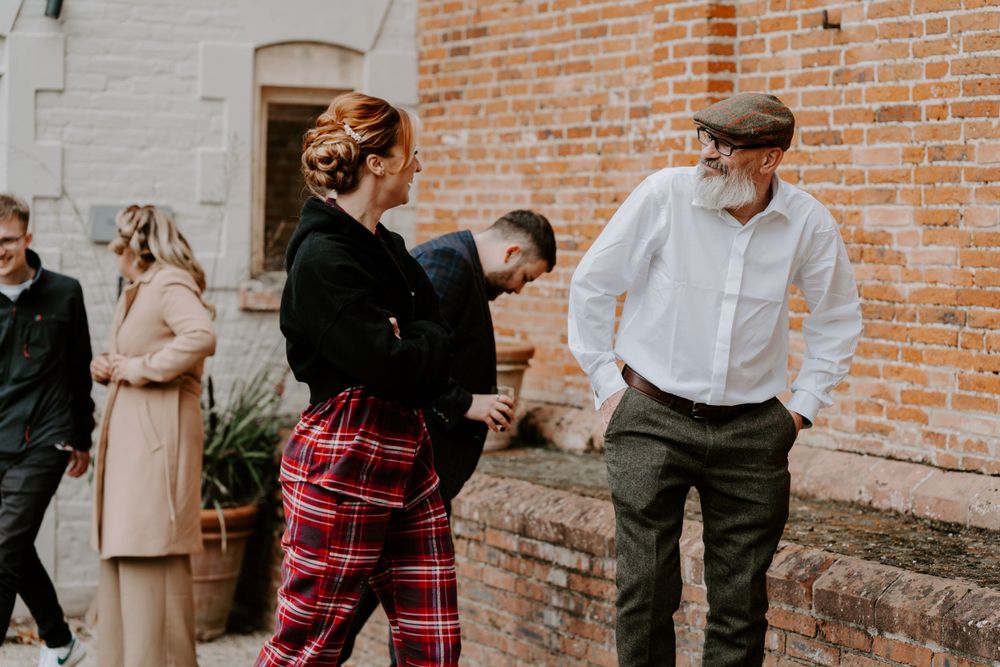 A bridesmaid is walking with her dad and they are smiling at each other. She is wearing red tartan pyjamas and her hair and make up is done