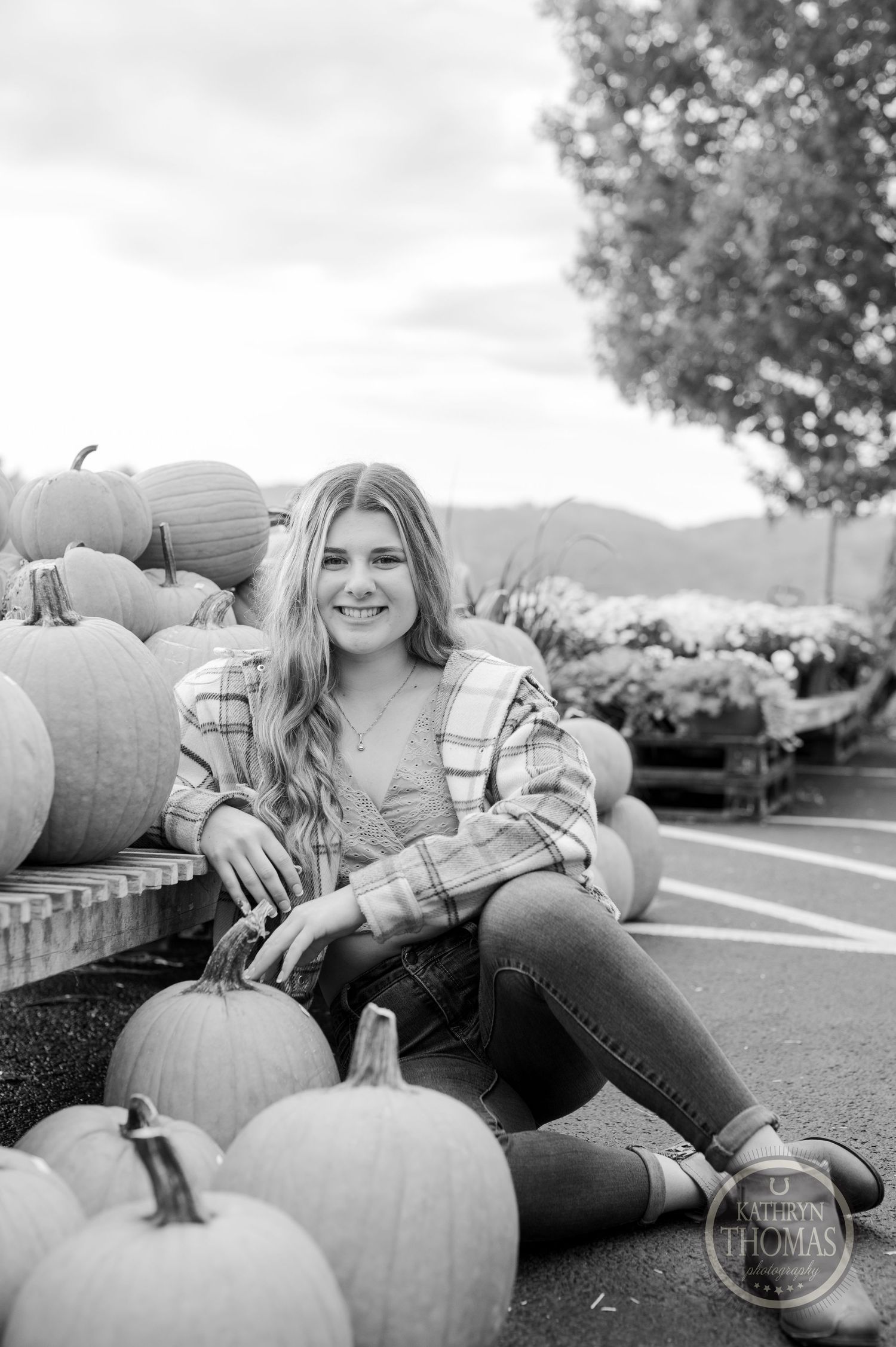 A black and white autumn portrait with someone sitting among pumpkins on display.