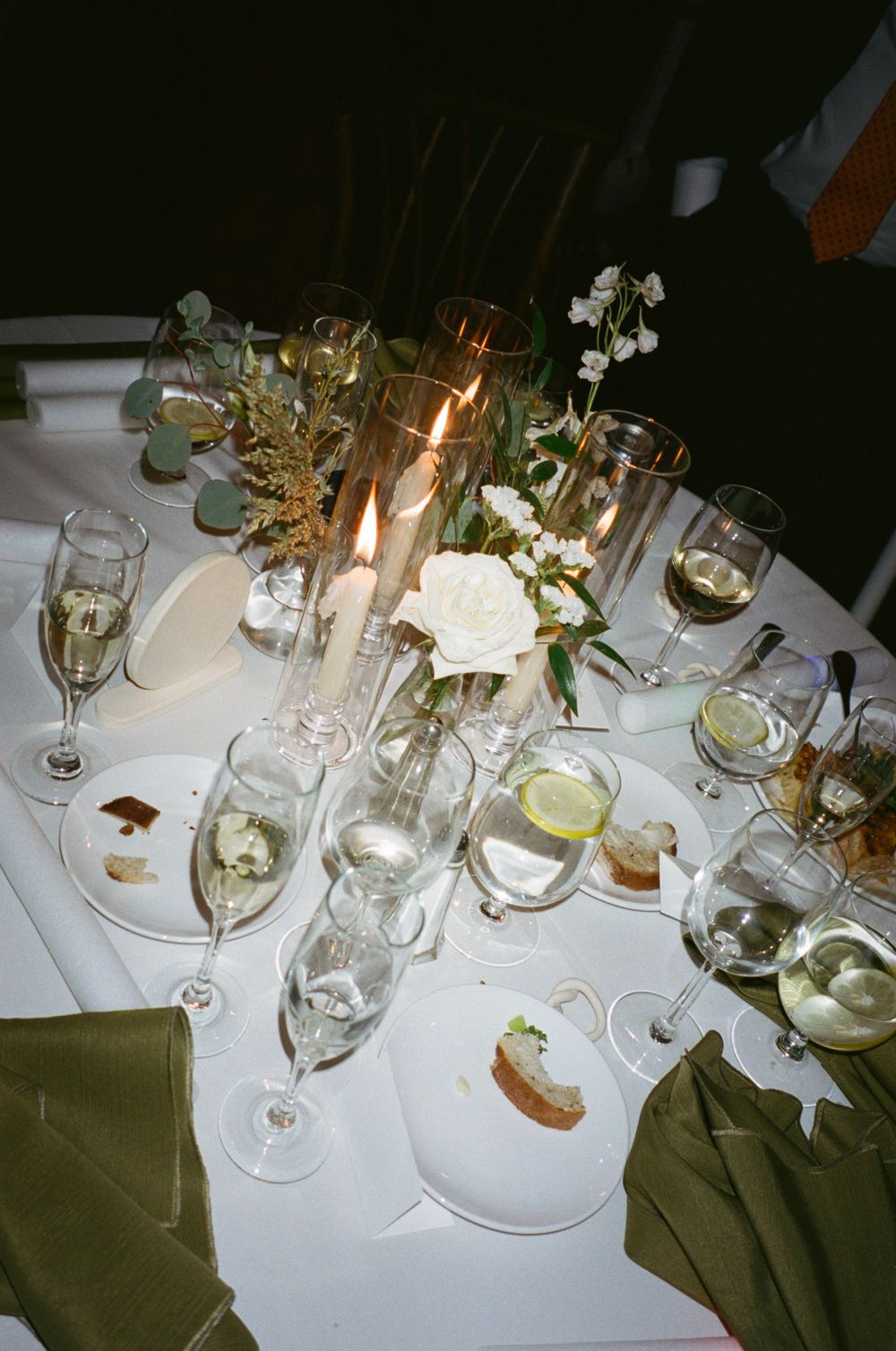 Elegant wedding reception table setting with candles, wine glasses, and white roses.