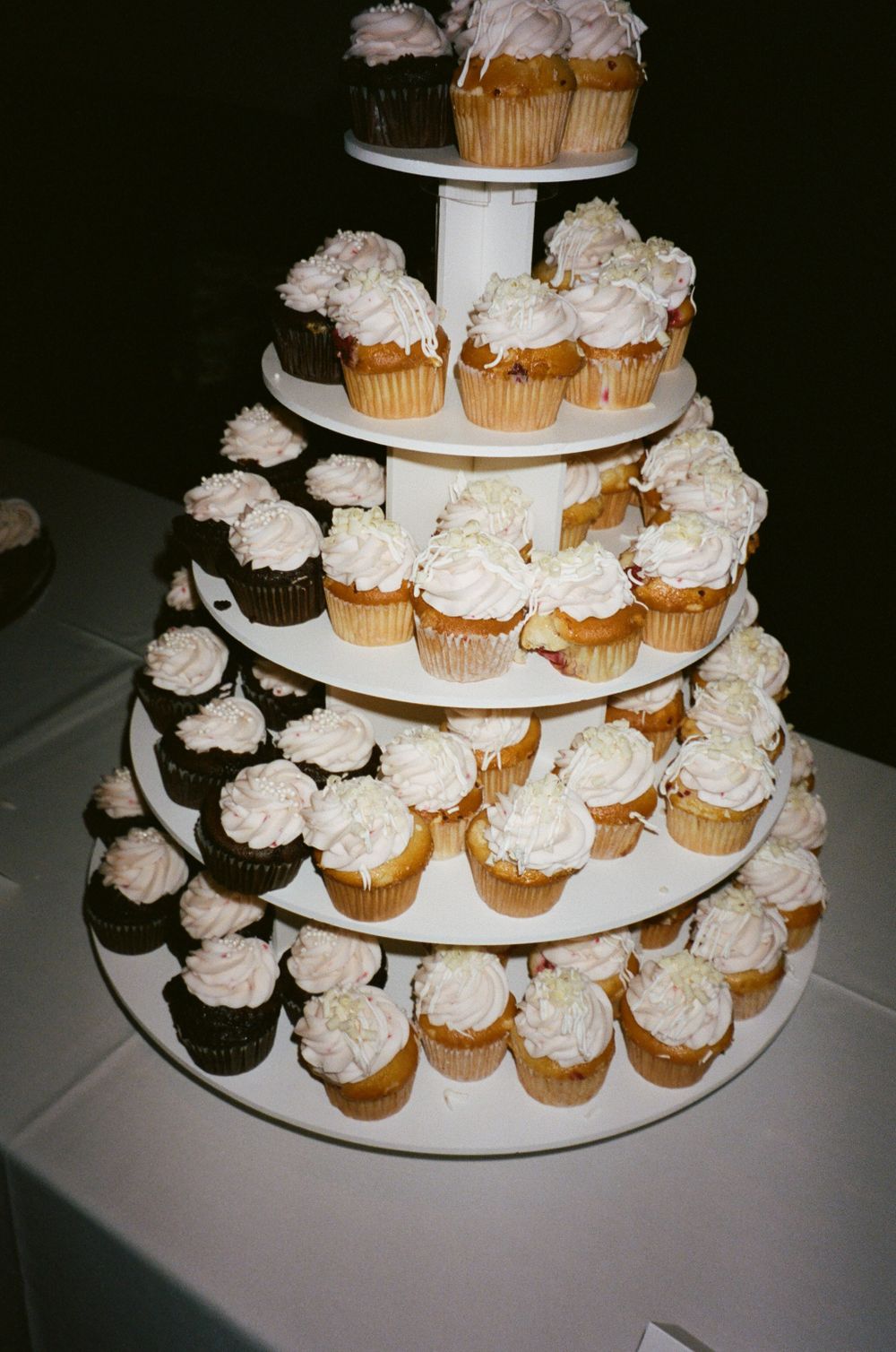 A five-tier display of wedding cupcakes with white frosting on a round stand.