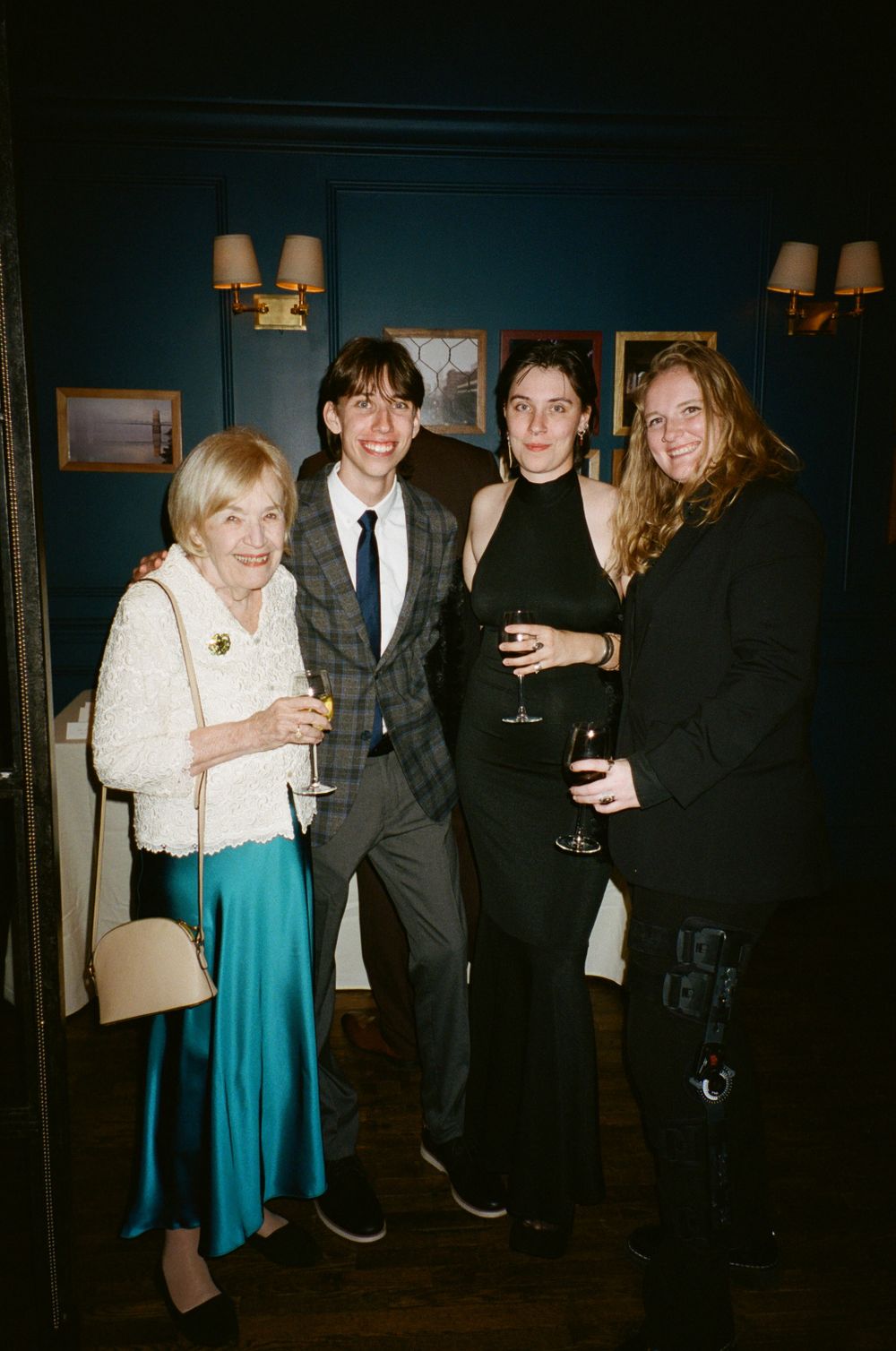 Four guests pose together at a formal event with wall sconces and dark decor in the background.