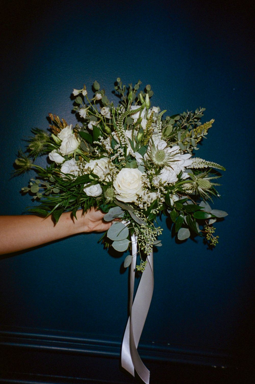 Elegant white and green wedding bouquet with roses and eucalyptus tied with ribbon.