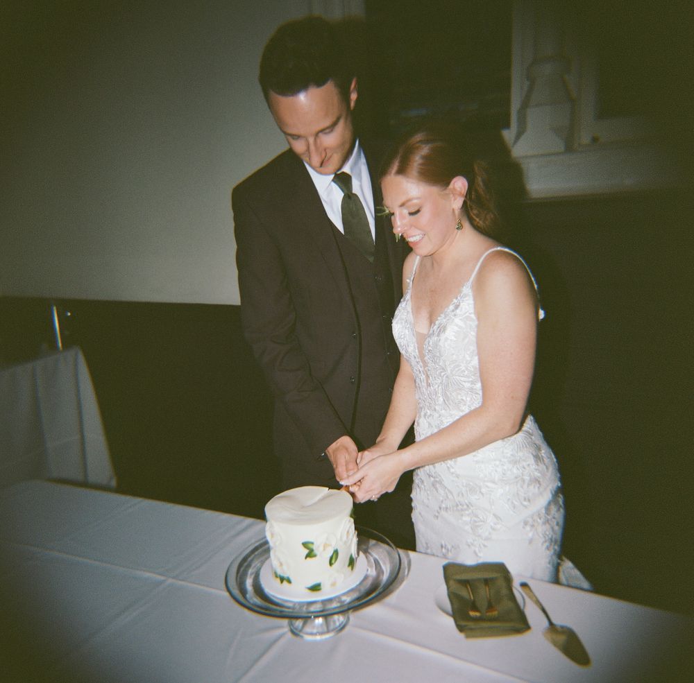 Couple cutting their small white wedding cake together at reception.