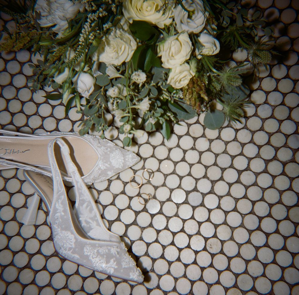 White sparkly bridal shoes next to floral arrangement on tiled floor.