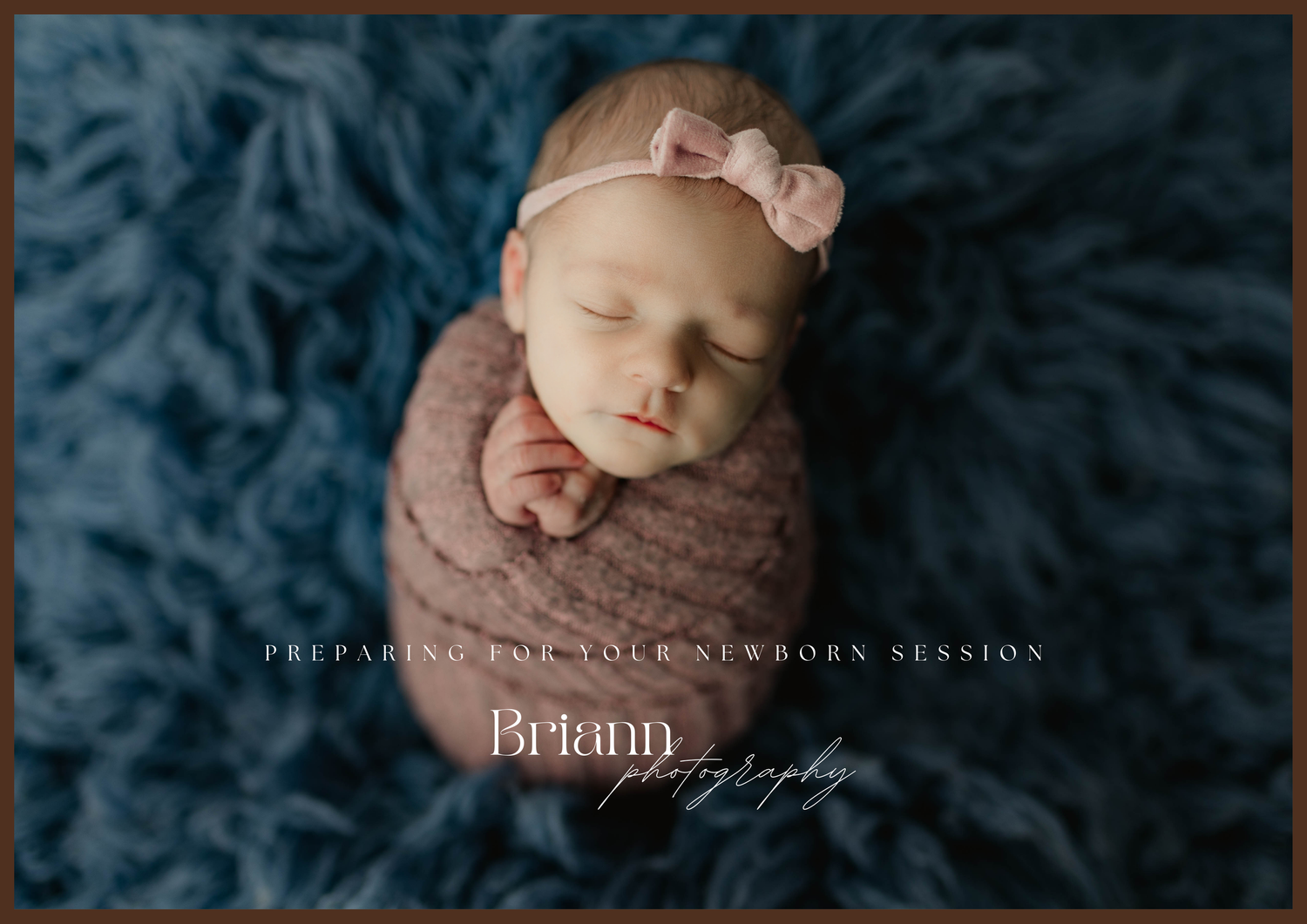 Newborn baby sleeping peacefully in mauve wrap with bow headband on blue textured backdrop.