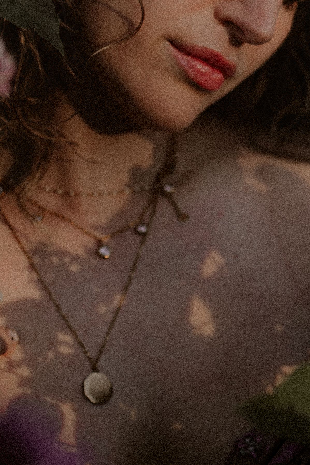 Woman wearing layered gold necklaces with a coin pendant, dappled light on skin.