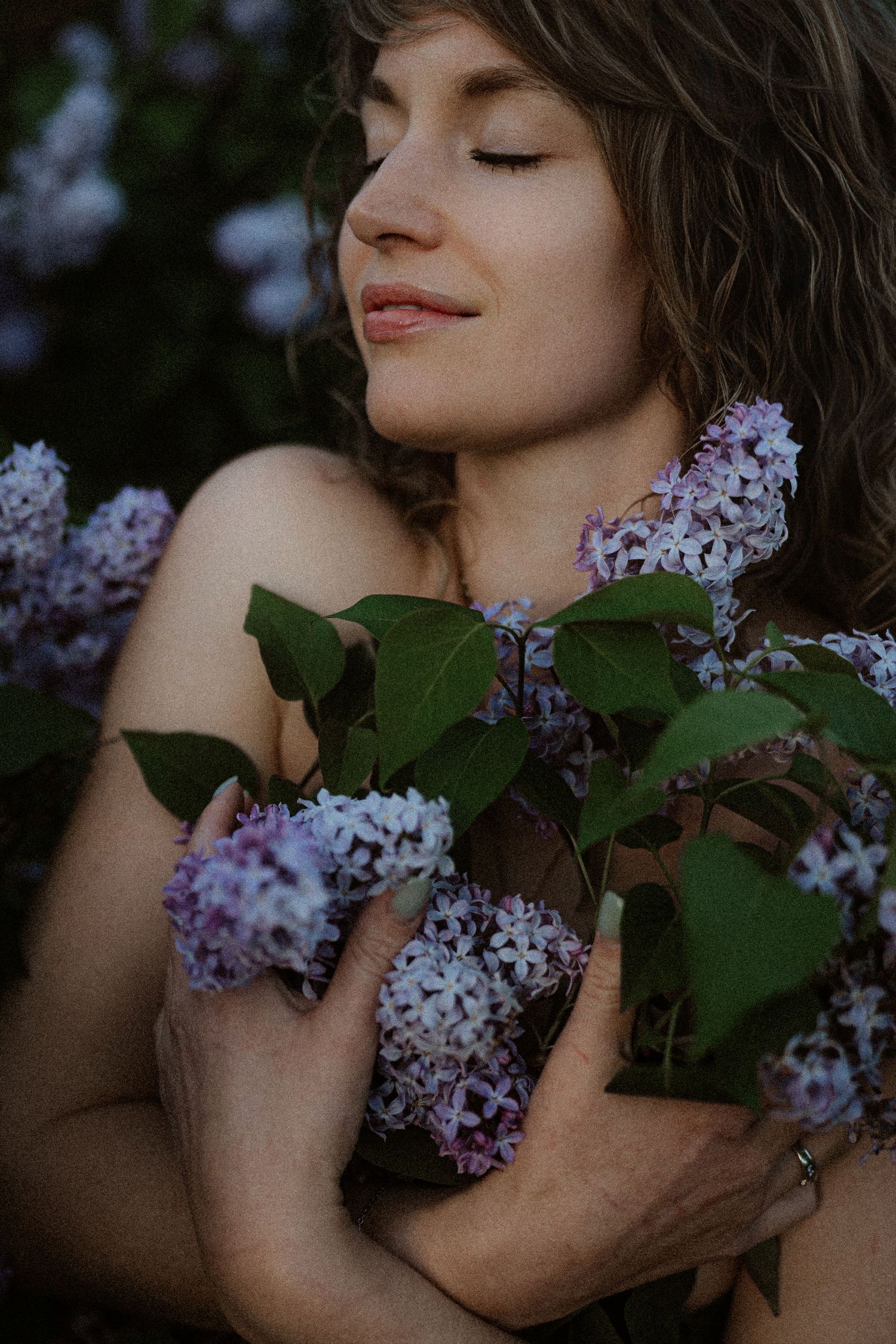 Woman with closed eyes peacefully embracing purple lilac flowers, serene nature portrait.