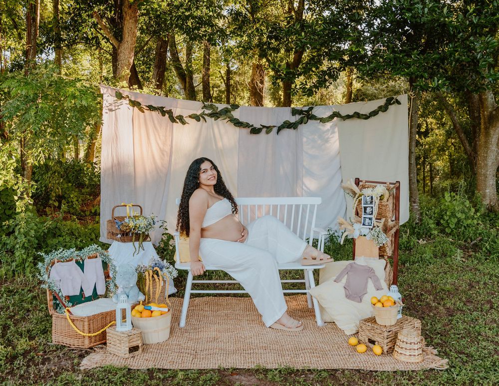 Outdoor maternity photoshoot setup with white backdrop and rustic decorations in a forest setting.