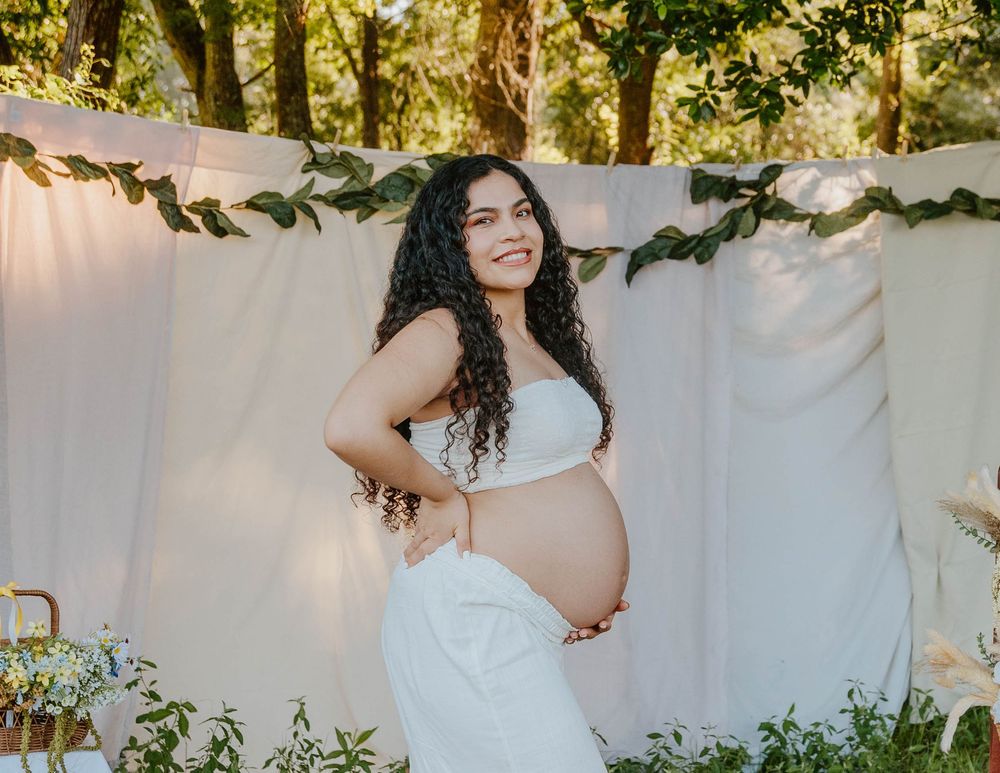 Maternity photo session with white backdrop and floral decorations in natural setting.