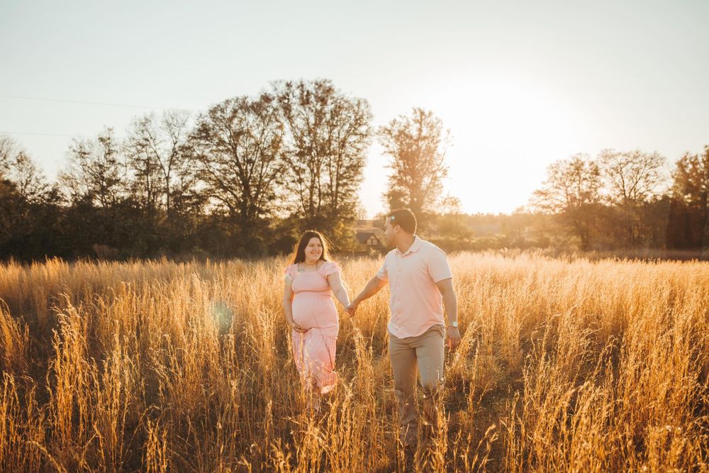 Silhouette of couple walking through tall grass field at sunset.