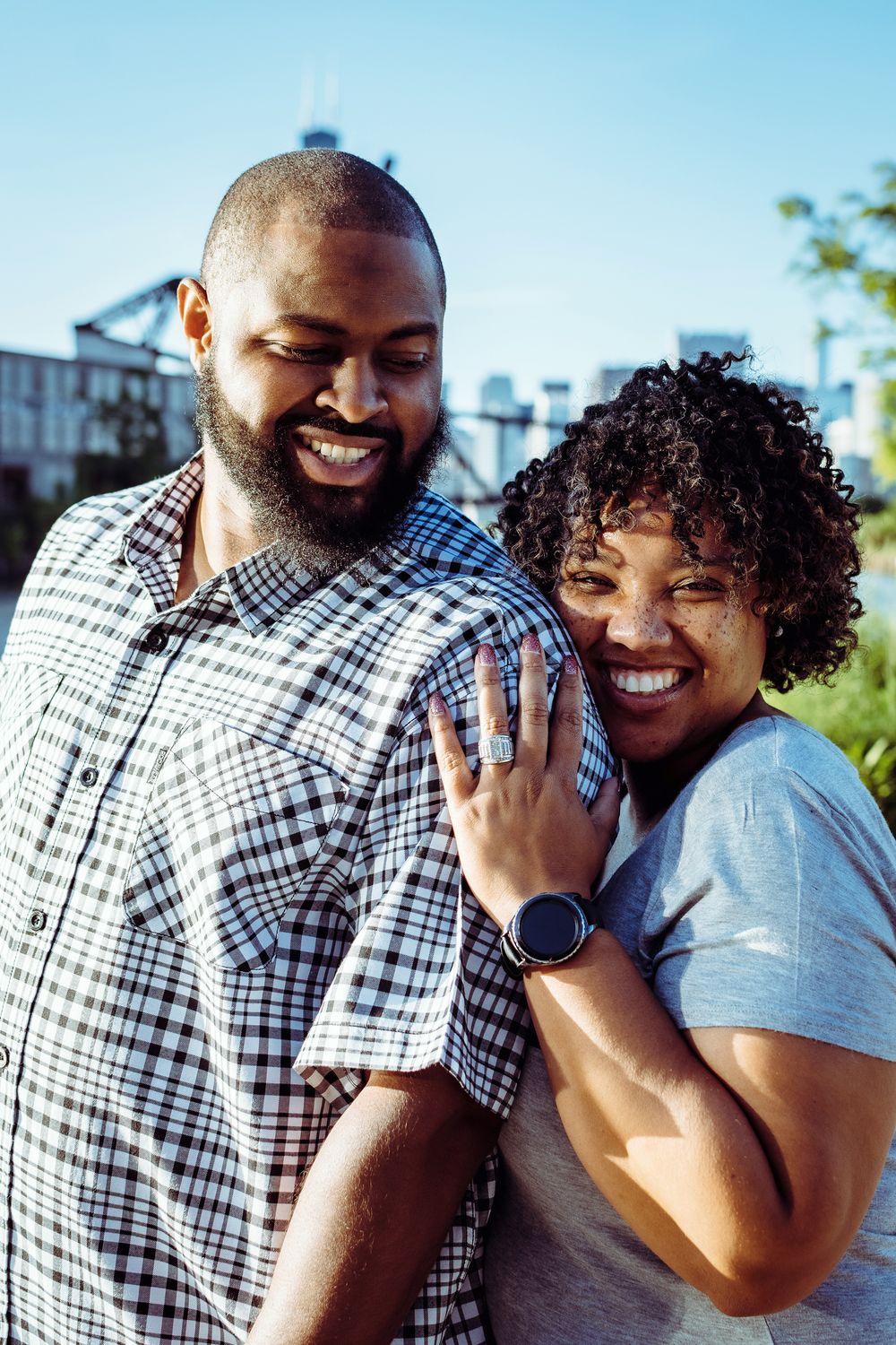 Happy couple showing off engagement ring in sunny outdoor setting.