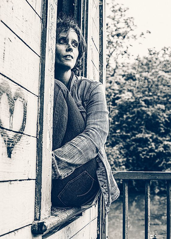 modernes schwarz/ weiß Portrait einer Frau in einem alten Bootshaus am Fenster sitzend mit Jeansjacke