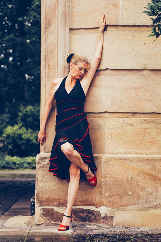 Stilvolles Bild einer Tänzerin in einem Tanzkleid und Tanzschuhen an eine Steinmauer gelehnt