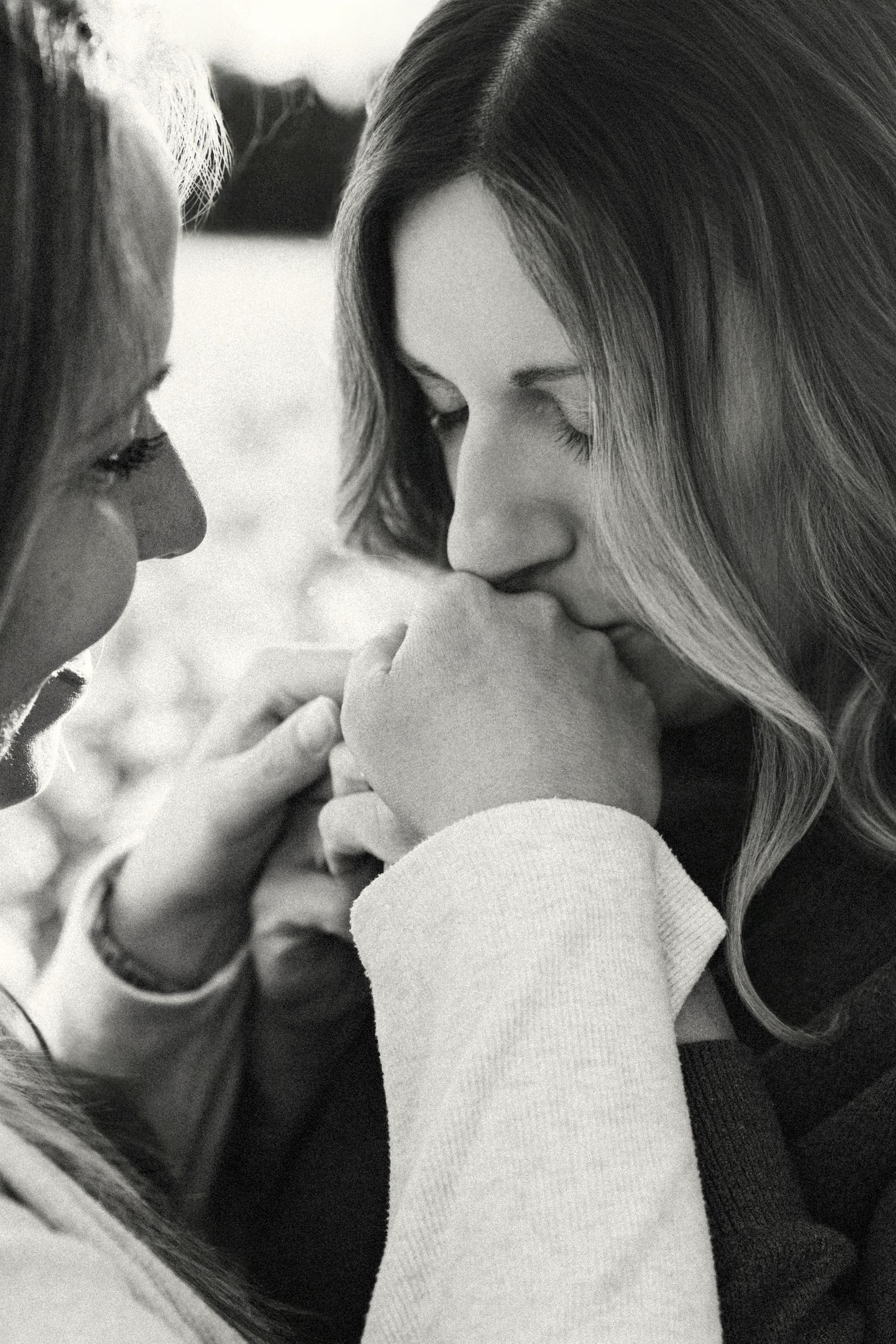 Black and white photo of two women sharing a tender moment, one kissing the other's hand affectionately.