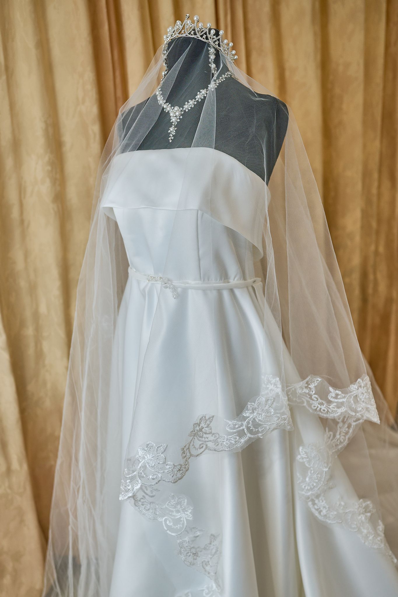 White wedding dress on a black mannequin with a necklace and veil.