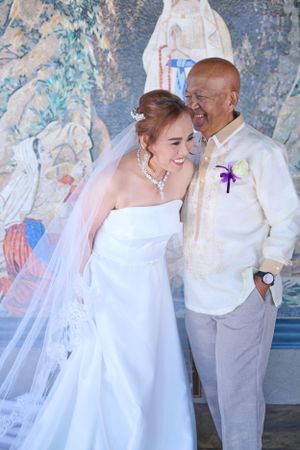Bride in a white dress and veil standing next to groom wearing a barong tagalog at St. Bernadette's Catholic Church in Stockton CA.