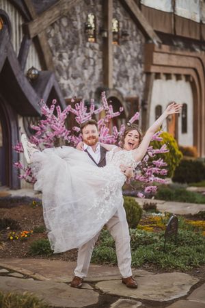 Happy newlyweds celebrate outdoors near stone building with blooming pink cherry blossoms in springtime.