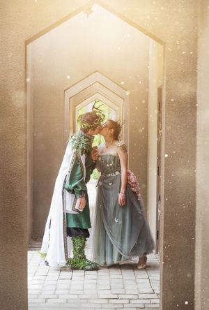 A romantic fantasy scene through archways with one figure in green regalia and another in a flowing blue-grey gown.