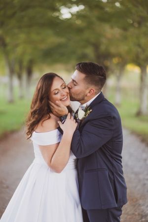Romantic moment captured on tree-lined path during wedding photoshoot.