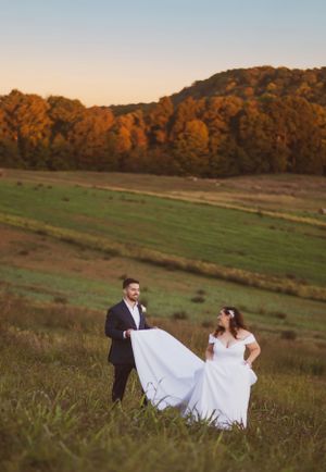 Couple in wedding attire playing with dress in golden sunset meadow landscape.