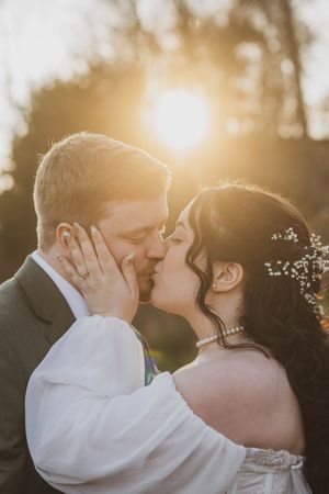 Romantic wedding photo capturing a kiss between a couple at sunset with golden light streaming through the trees.