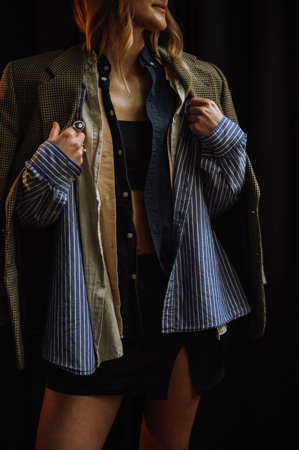 Fashion shot featuring layered outfit with striped shirt and olive jacket in moody lighting.