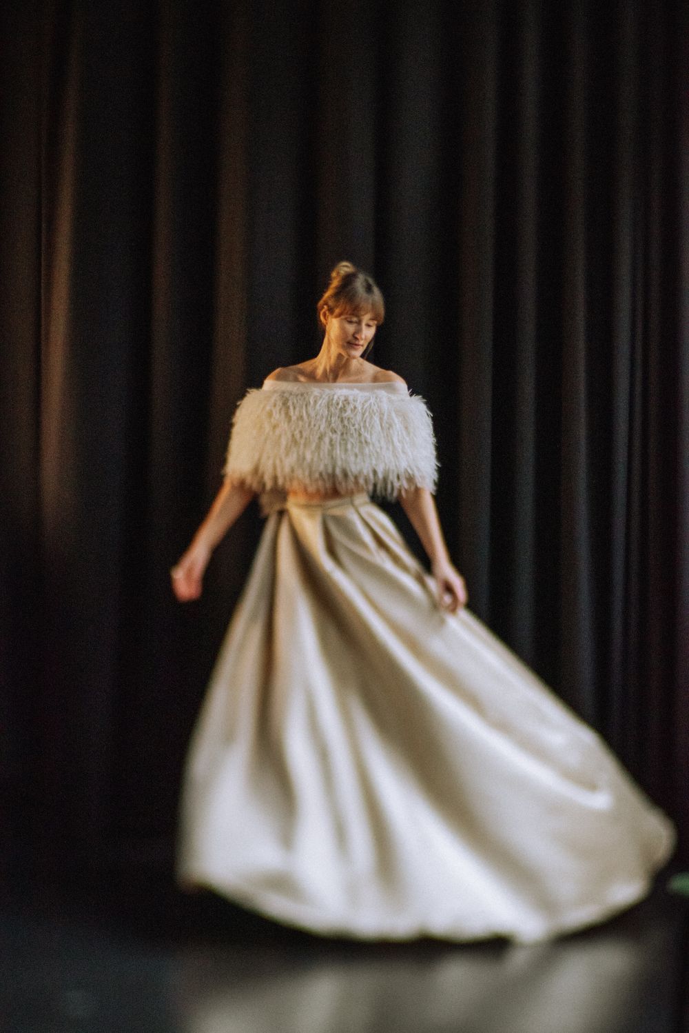 Elegant white dress with feather trim twirls against dark theatrical backdrop.