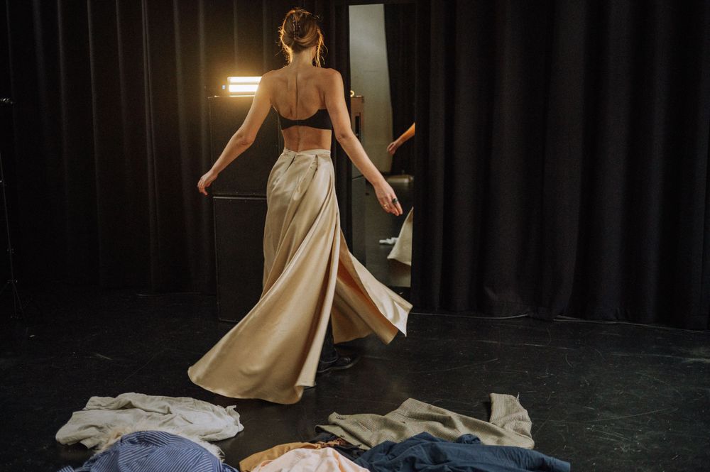 Flowing cream dress twirls gracefully against black theater curtains.
