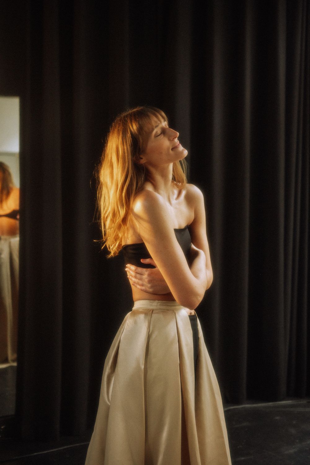 Artistic portrait of dancer in cream dress against dark theater curtains.