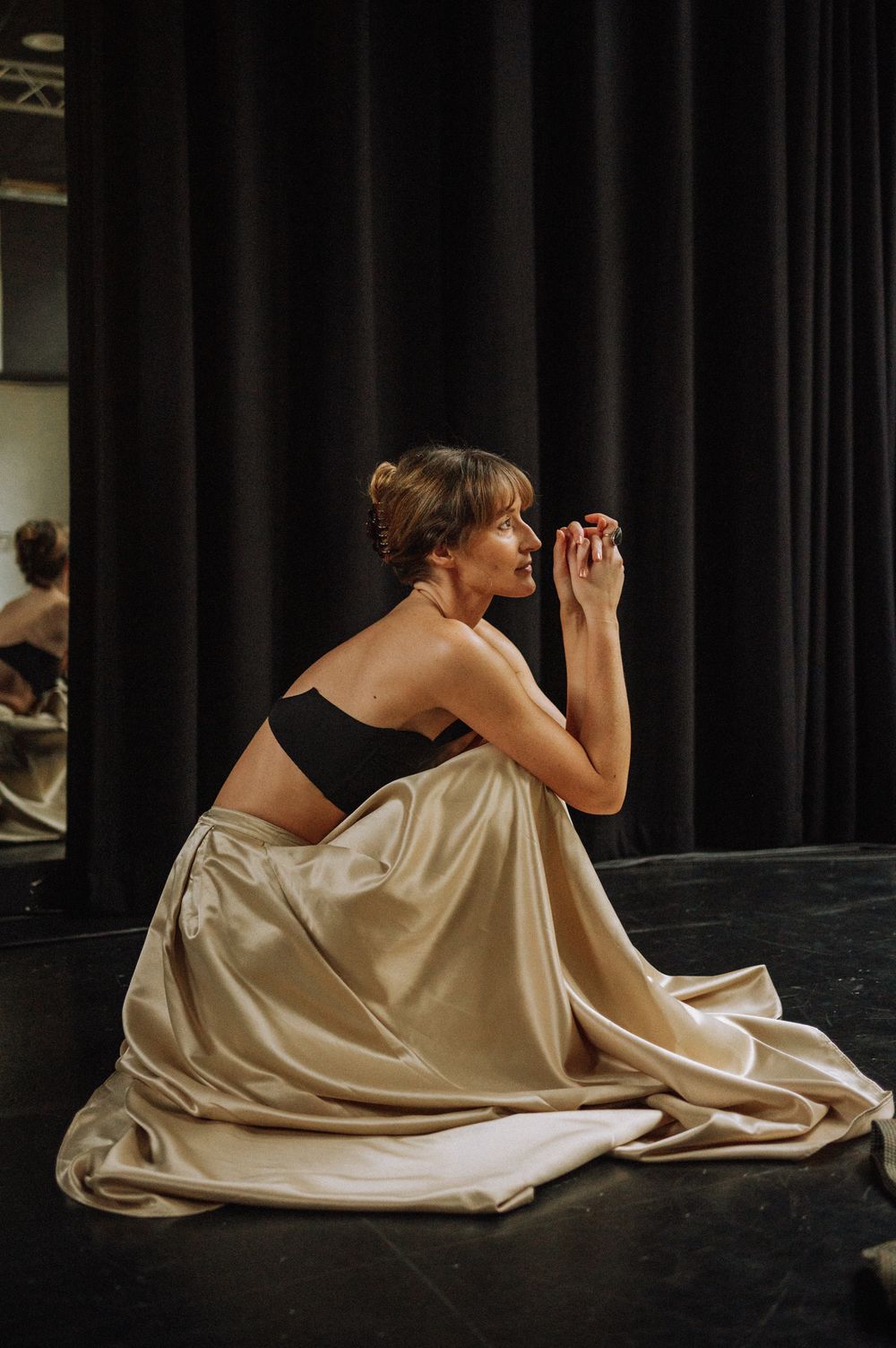 Elegant reclining pose in champagne colored dress on dark stage floor.