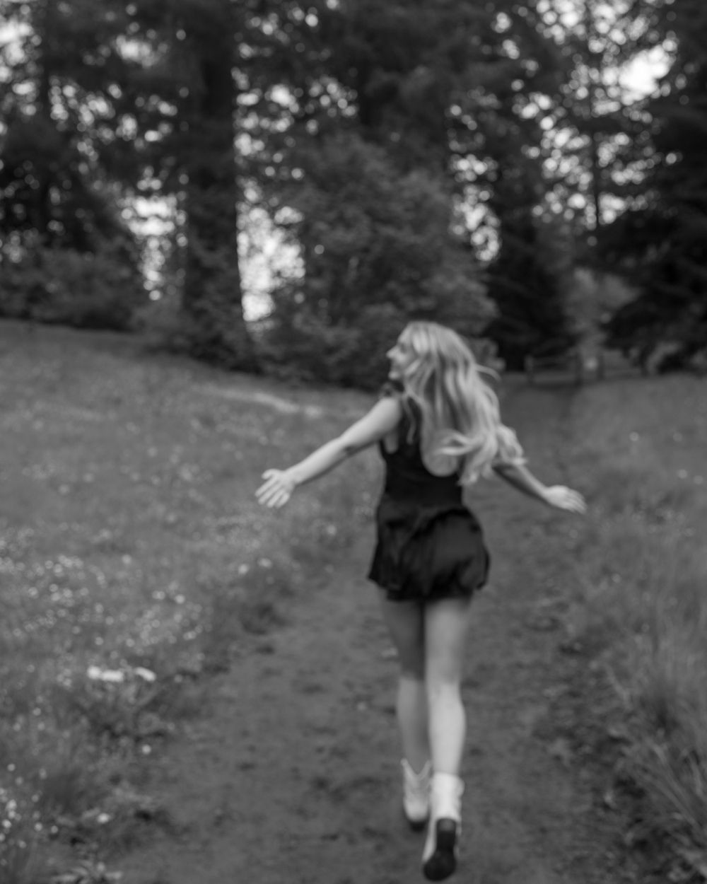 Highschool senior girl twirls gracefully on forest path in black and white photograph.