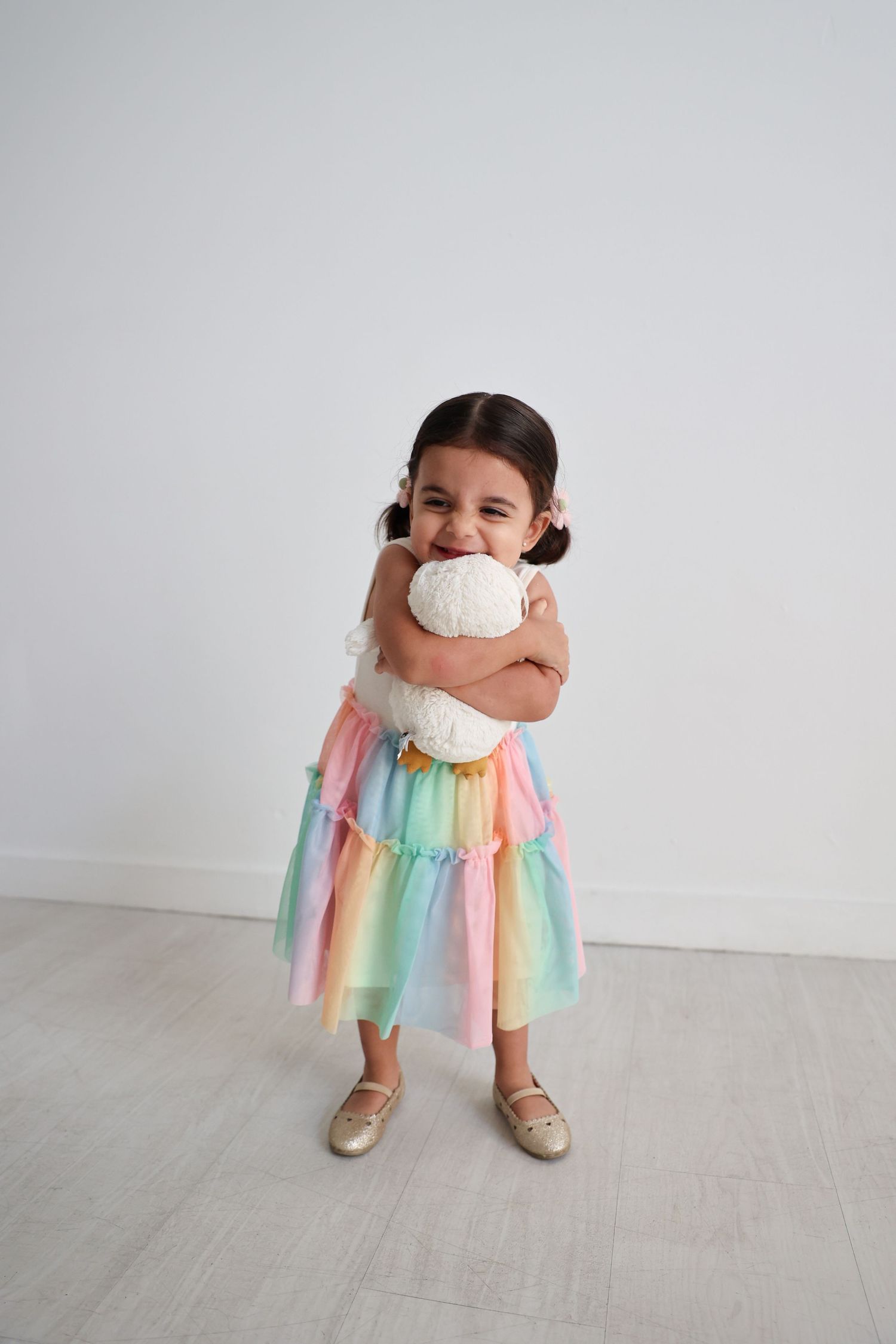 A small child in a rainbow tulle dress hugs a white owl against a light background at the photography studio, The Lumen Room, in Austin, TX.