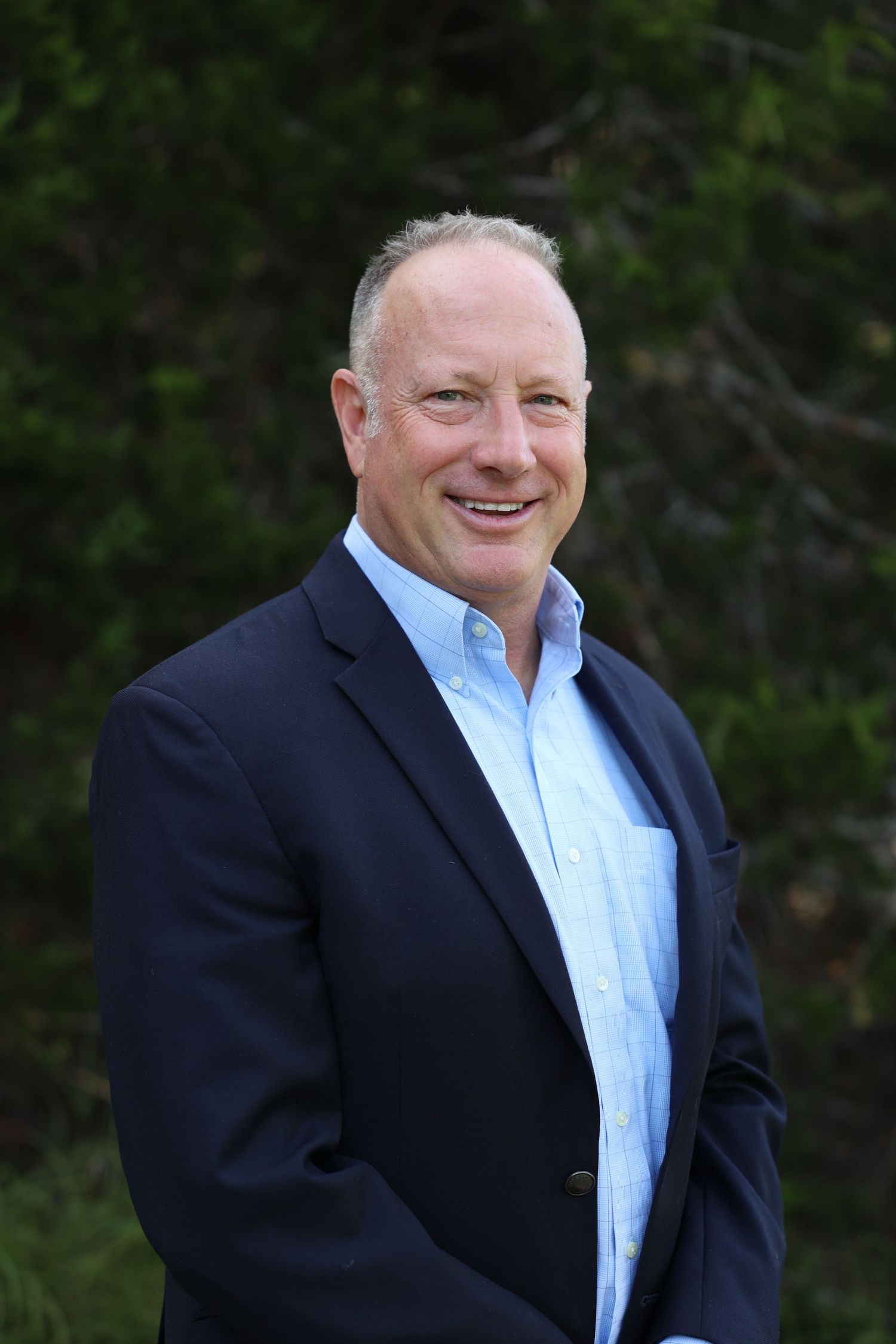 A professional in a navy suit and light blue shirt smiling against a green backdrop.