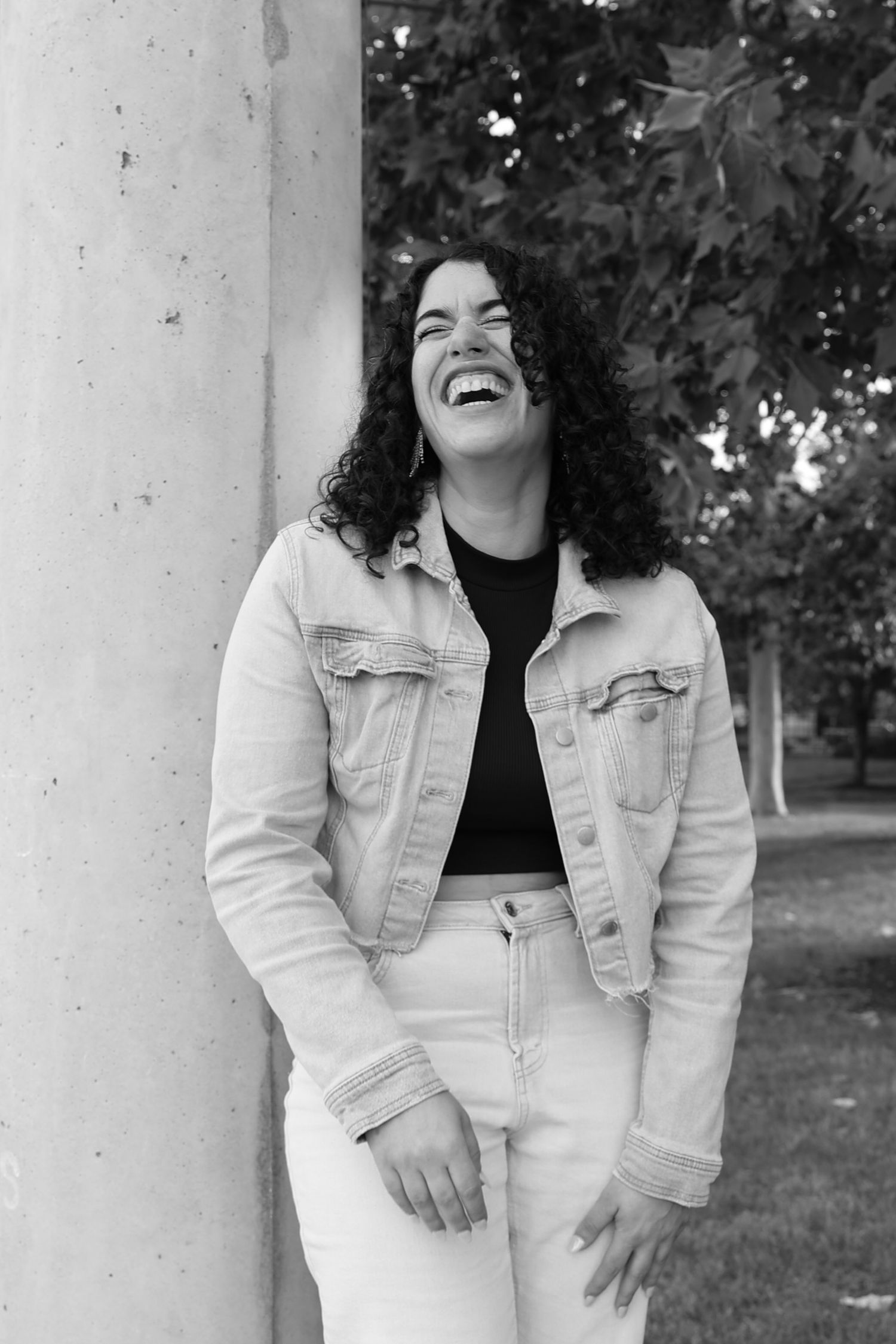 A casual black and white portrait showing joyful laughter while wearing denim jacket.