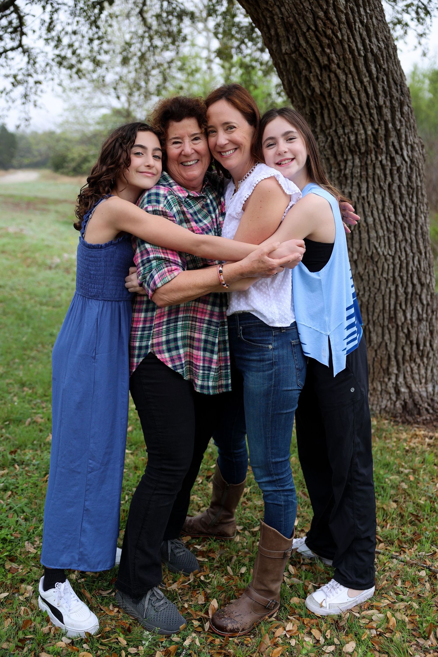 A group of four people share a warm embrace while standing under a large tree.