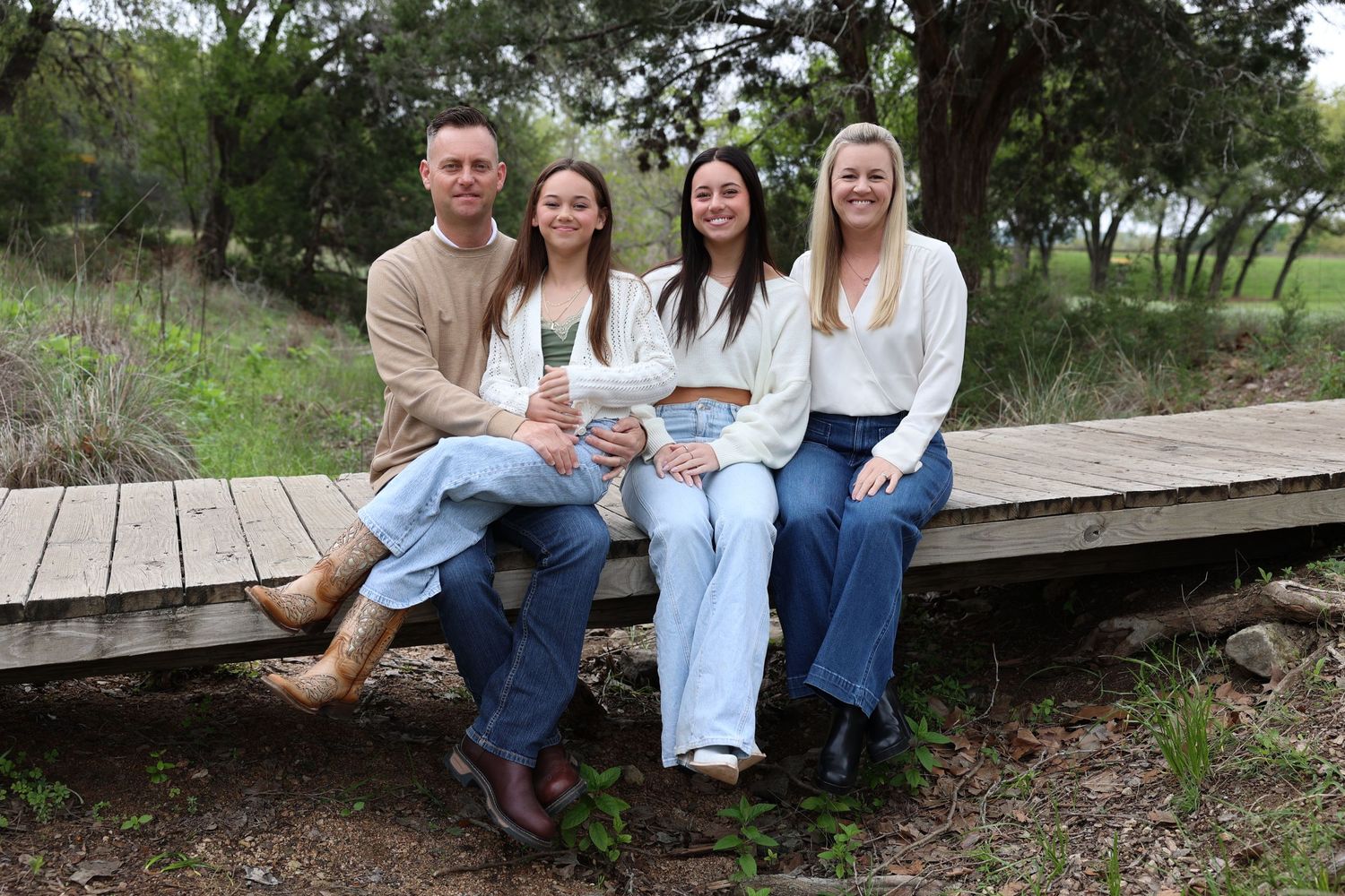Group of four family members sitting casually on wooden deck in natural setting.