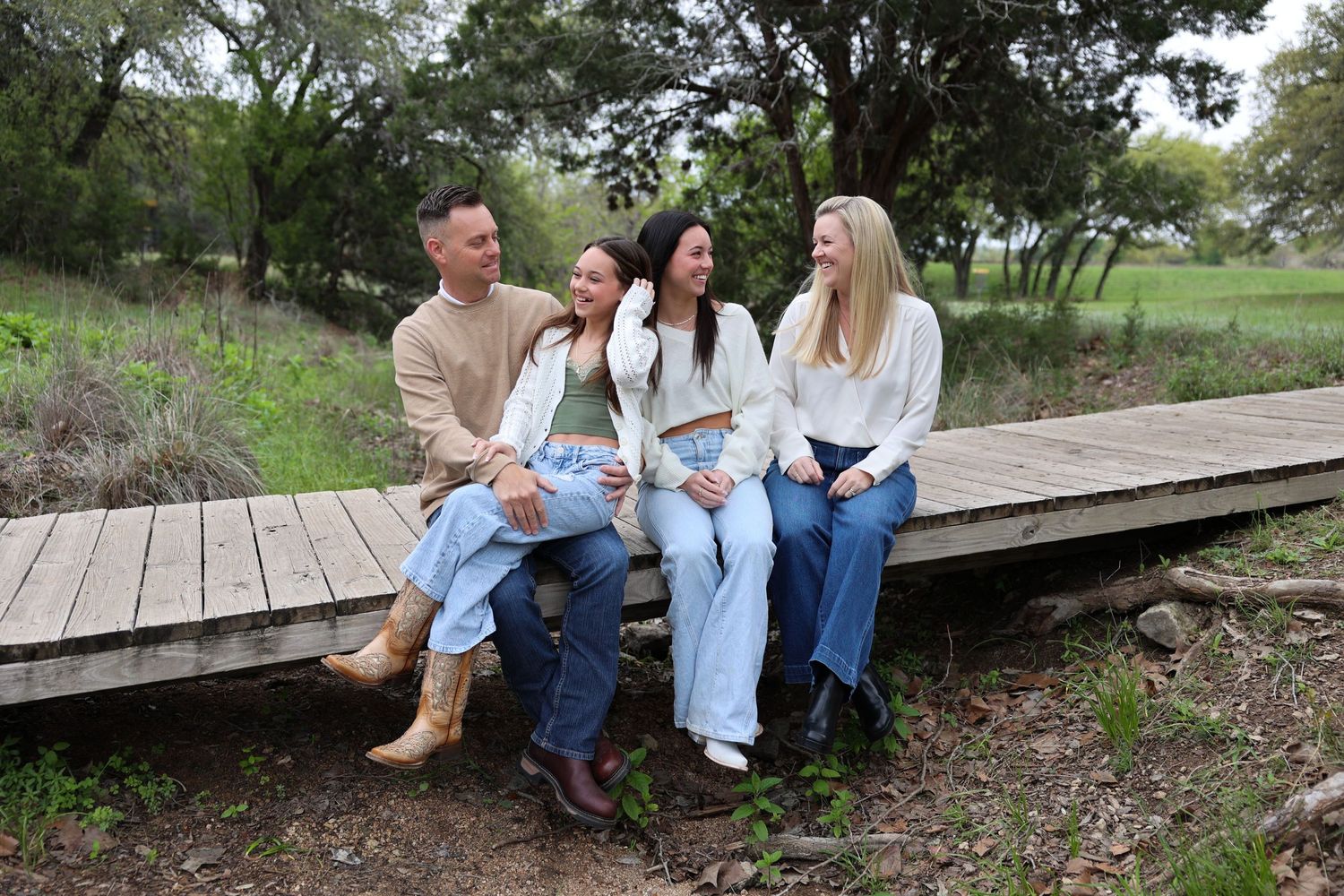 Four family members in casual attire sitting together on wooden boardwalk outdoors.