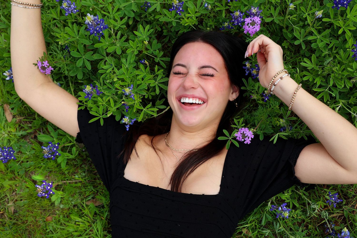 A grad lies in a field of purple flowers while laughing joyfully for her senior photos.