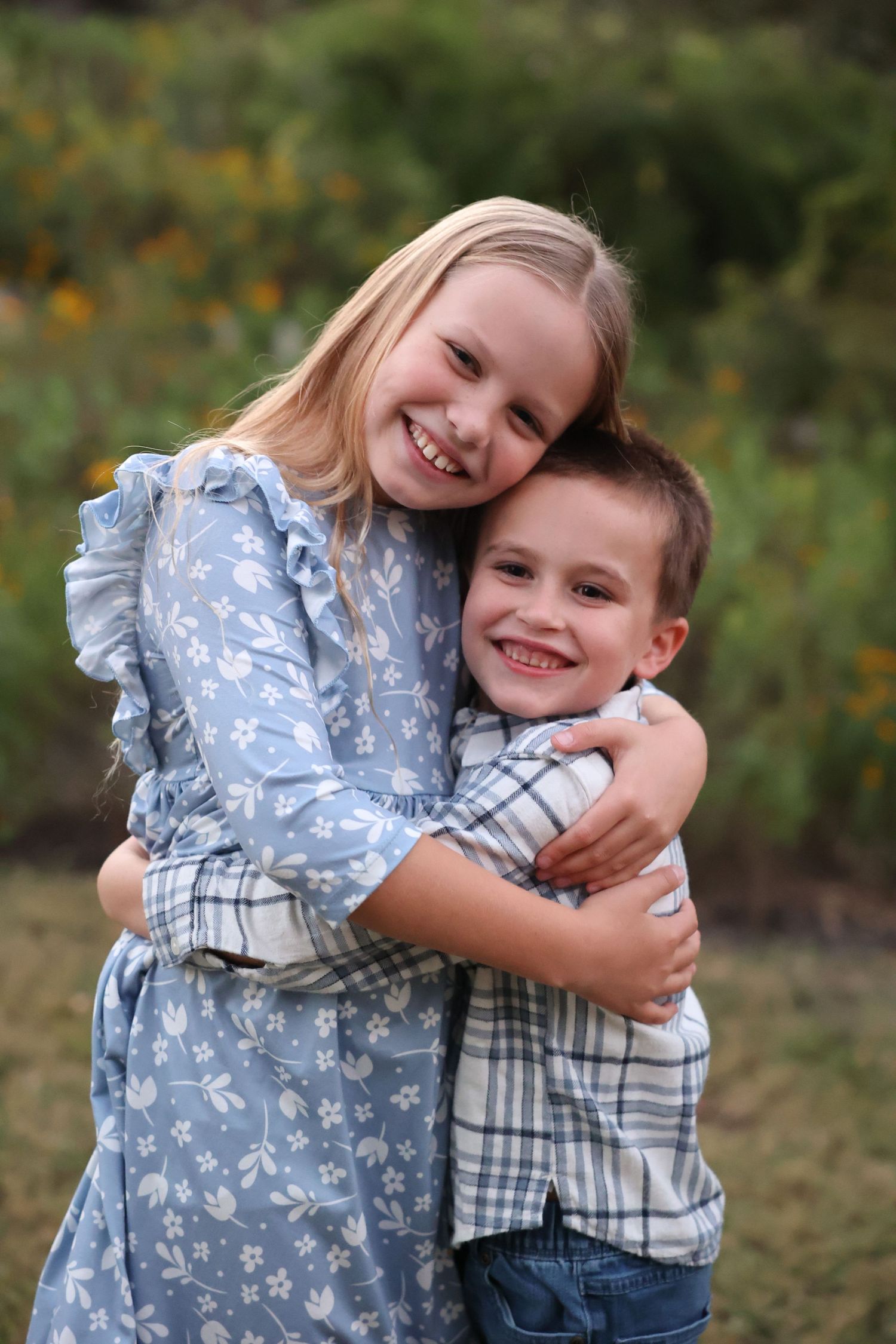 Two children embrace and smile while posing outdoors in casual clothing for family photography mini session in Bee Cave, TX.