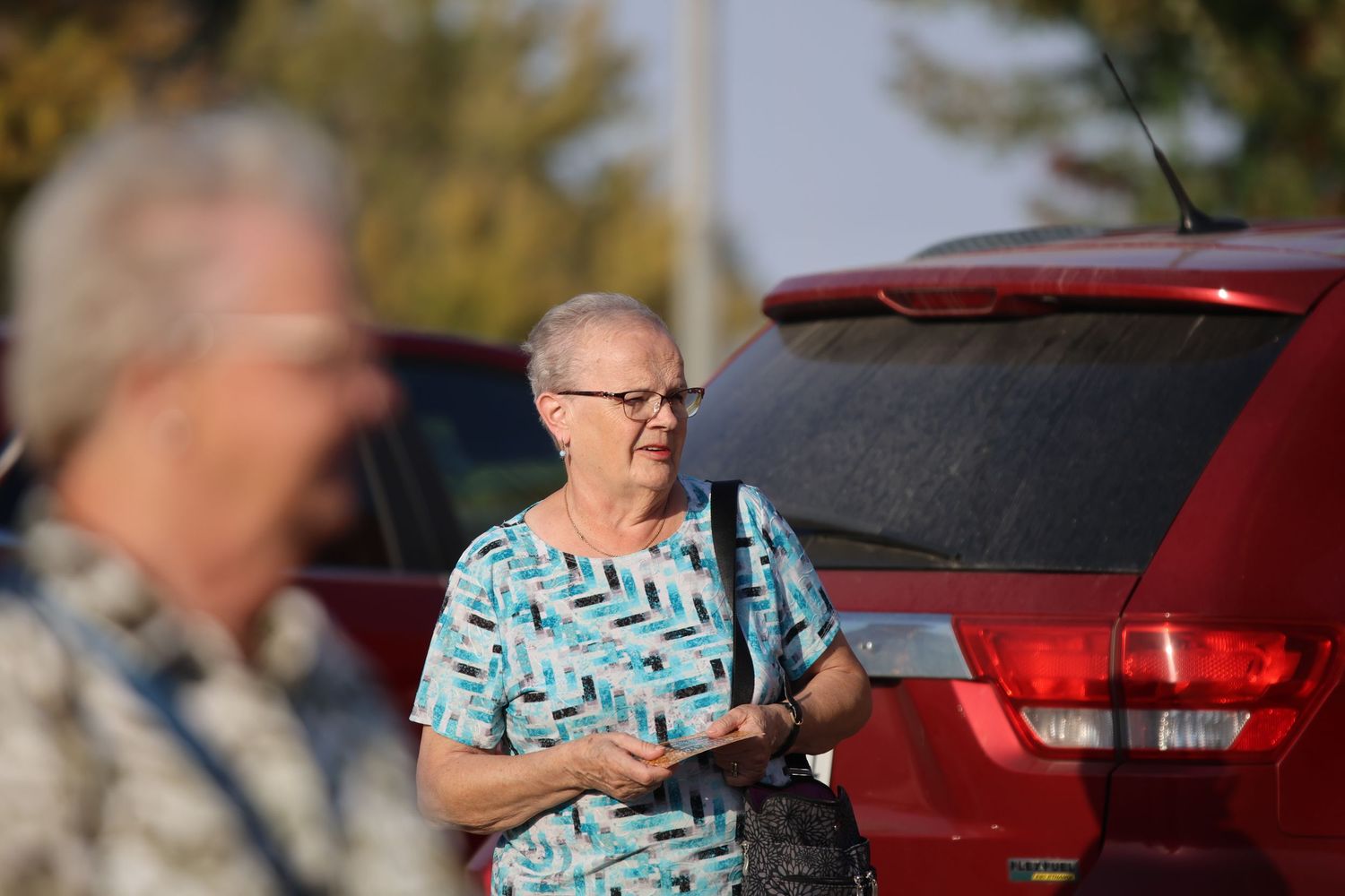 Person in turquoise shirt standing next to red vehicle in parking lot.