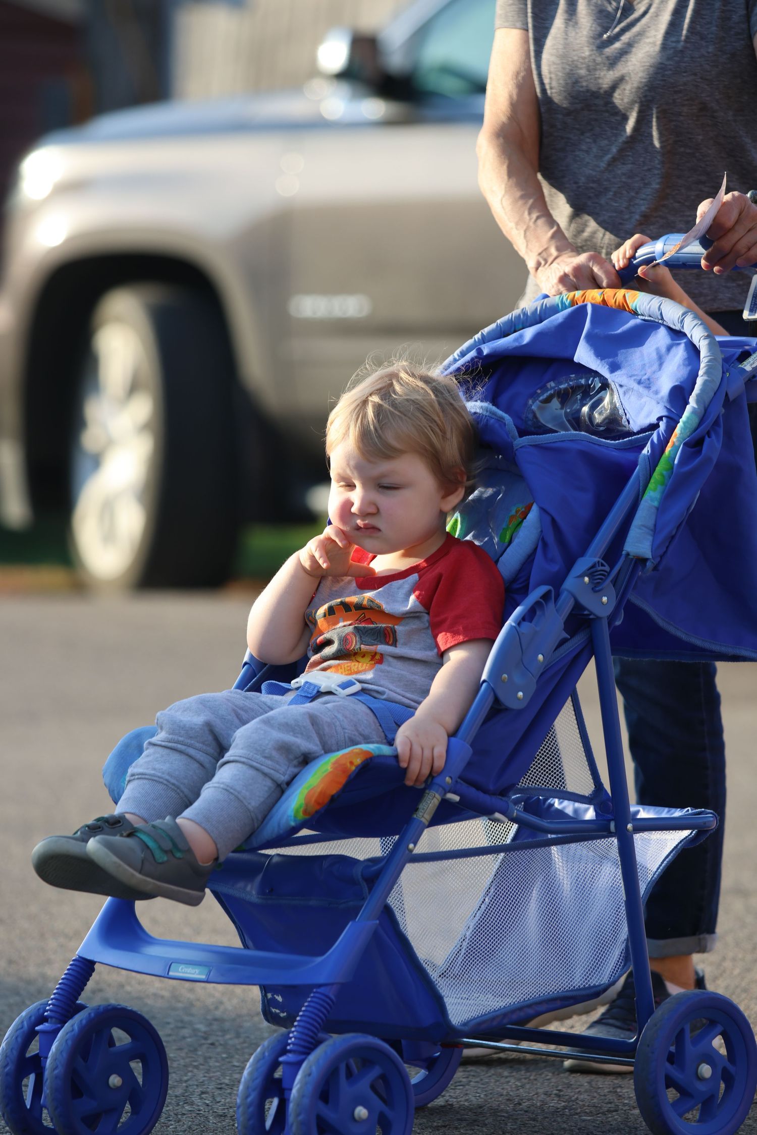 Child relaxing in blue stroller during outdoor event.