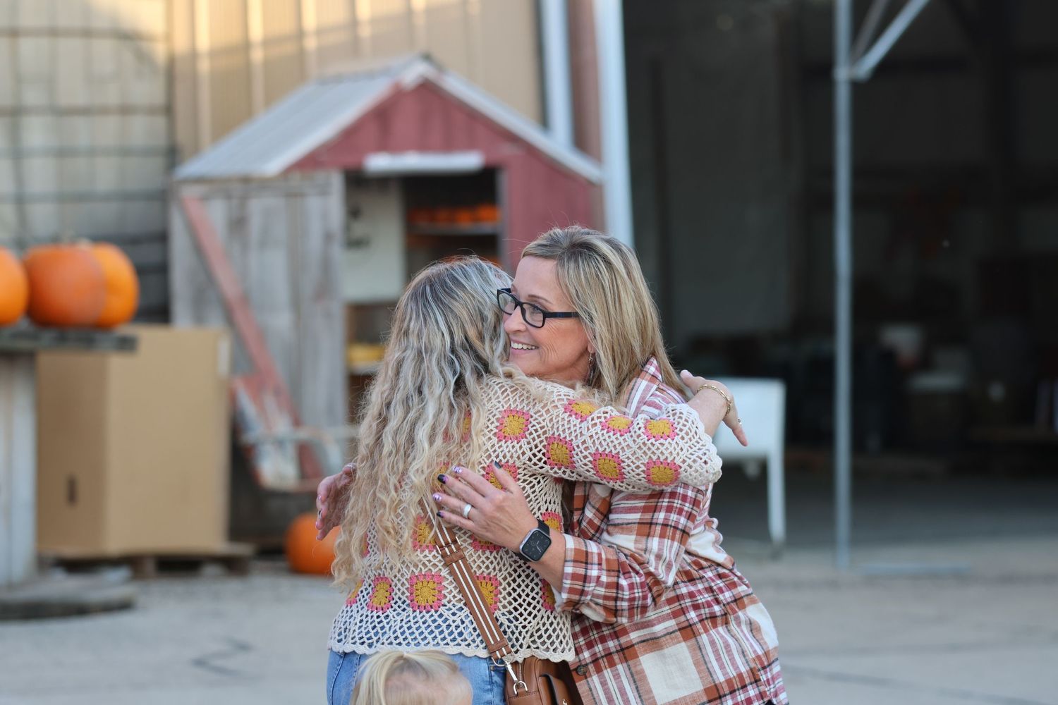 Two people share an embrace outside a red barn with pumpkins visible in the background.