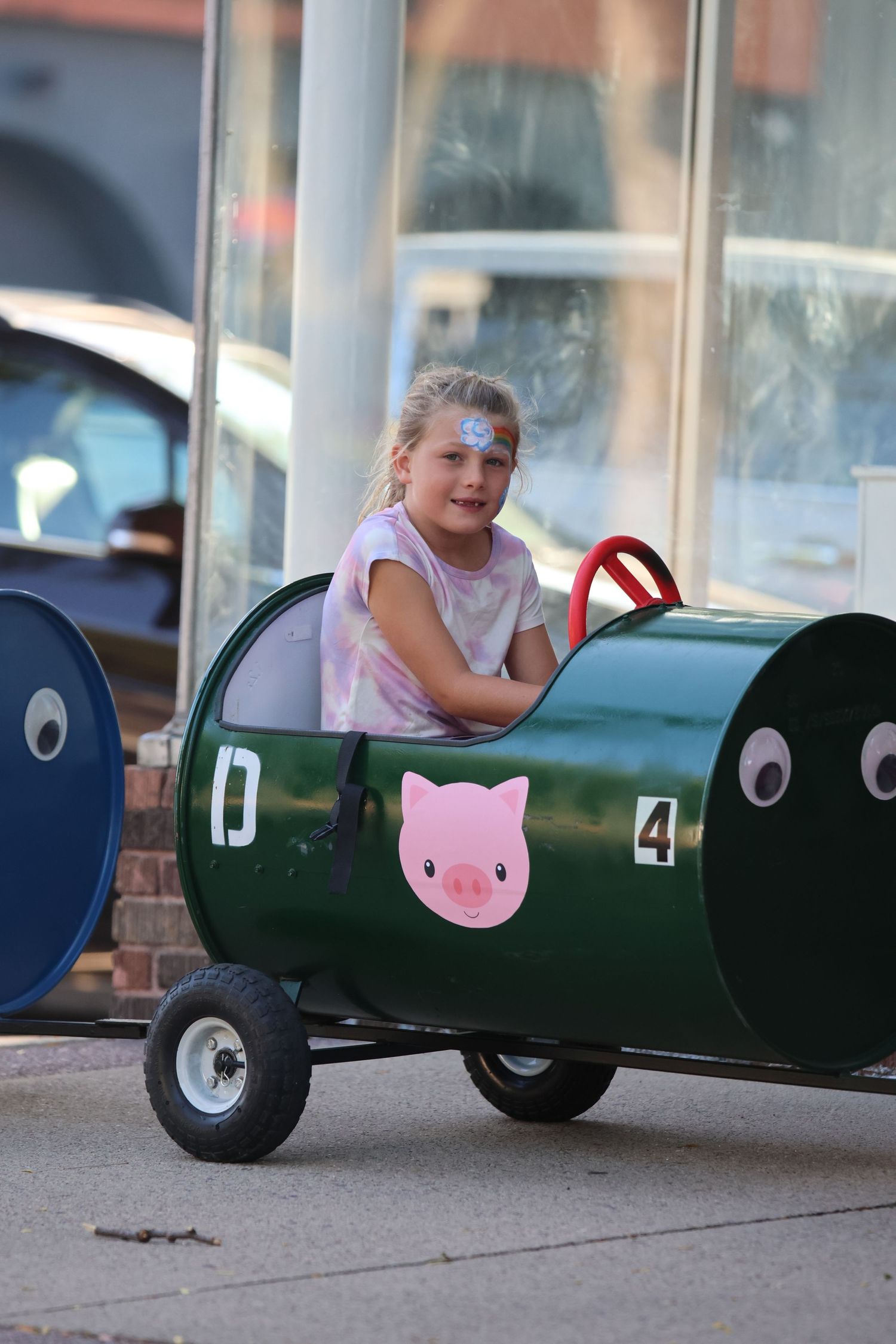 A toy barrel car painted green with a pink pig decal parked outside a building.