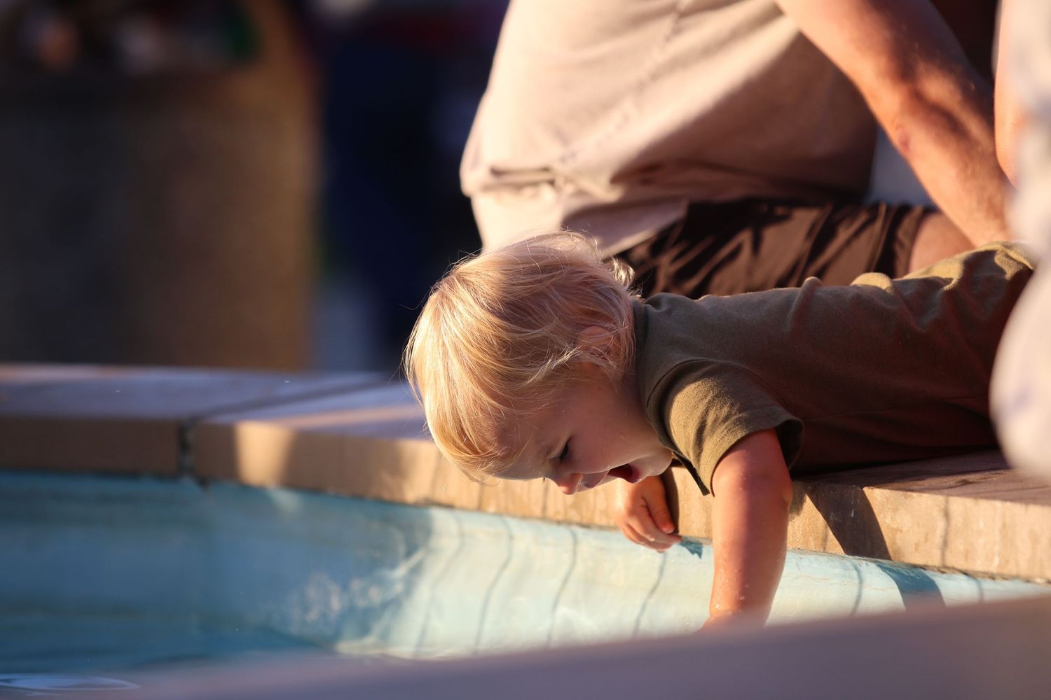 A child peering into water in golden afternoon sunlight.
