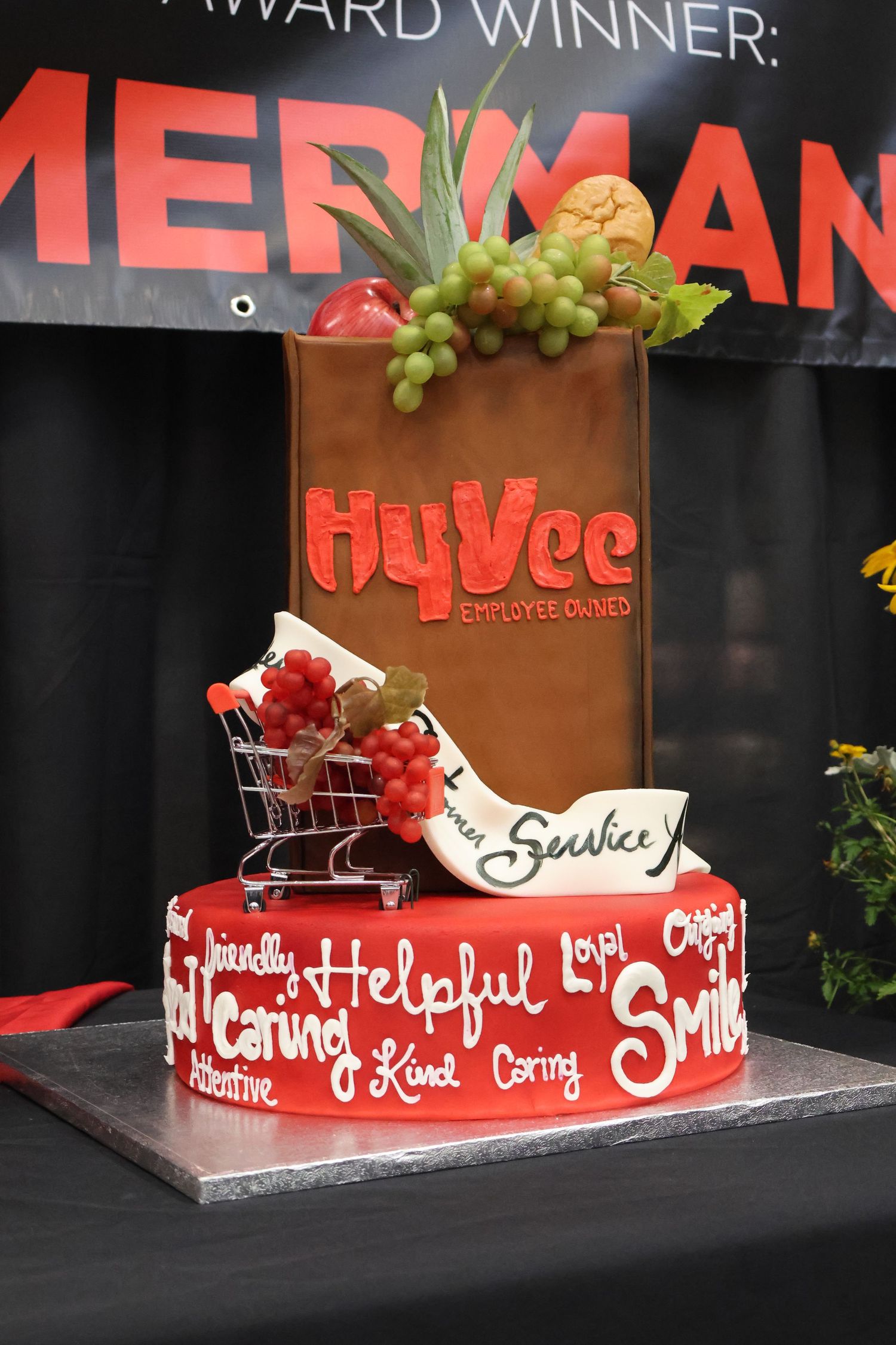 Decorative cake featuring HyVee logo, shopping cart, and fresh fruit decorations.