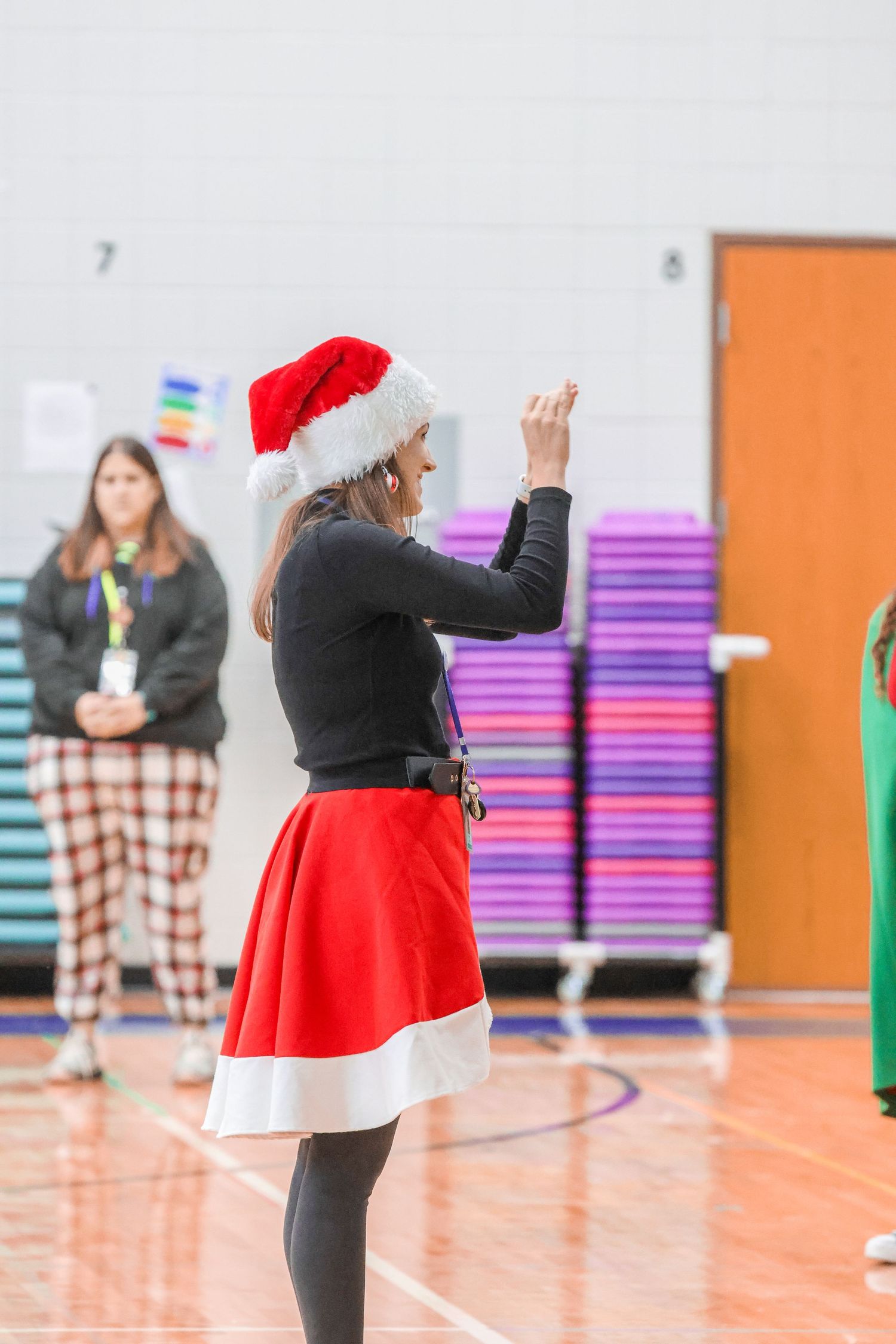 A performer in Santa-inspired costume leads a holiday performance in a gymnasium.