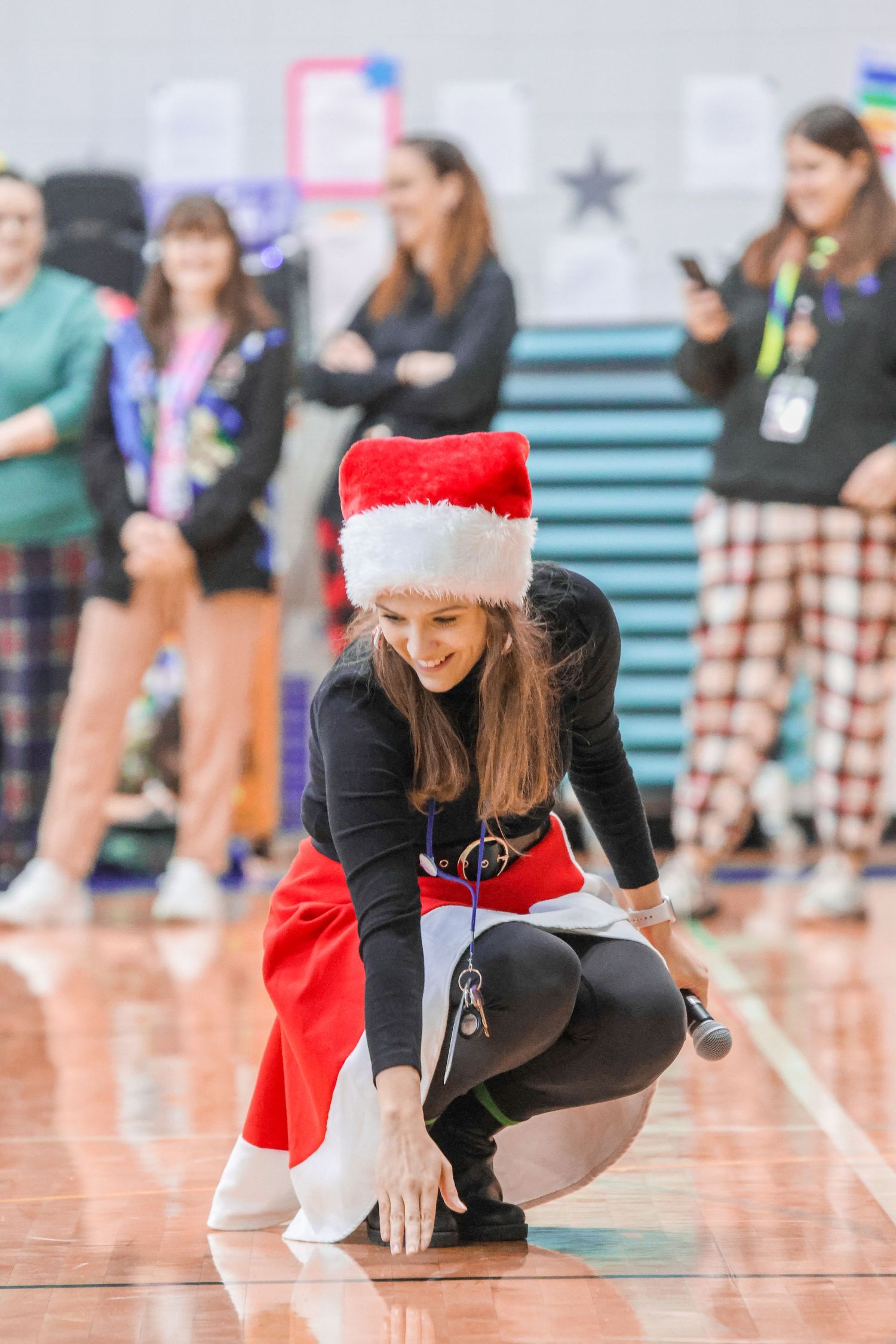 A performer in holiday attire crouches on a gymnasium floor during a show.