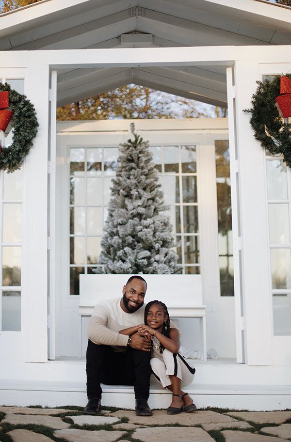 Father and daughter interlocking arms and sitting in front of a glasshouse.