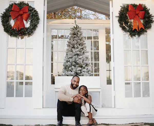 Father and daughter interlocking arms and sitting outside of glasshouse for Christmas.